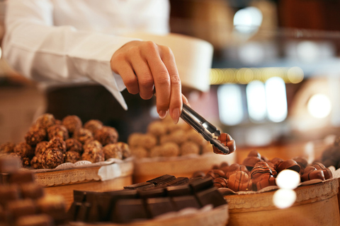 Un chocolatier saisissant une praline parmi un assortiment de chocolats dans une boutique de Bayonne.