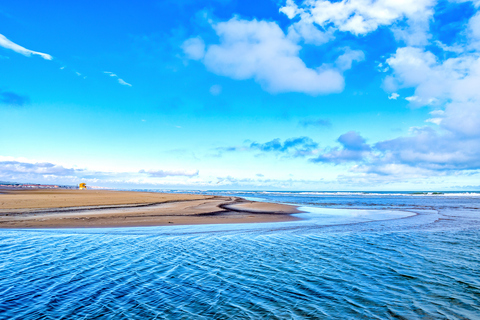 Une large plage de Narbonne bordée par la mer sous un ciel bleu parsemé de nuages.