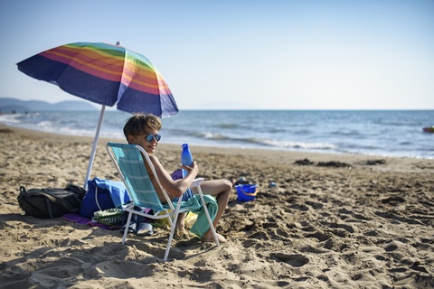 Un enfant assis sous un parasol sur une plage de Narbonne, face à la mer.