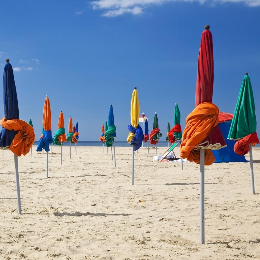 Des parasols colorés fermés sur une plage de sable en Normandie.