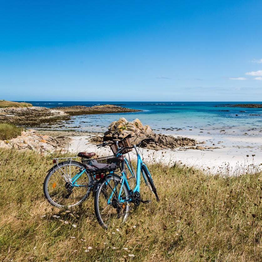 Deux vélos posés face à une plage rocheuse et à la mer en Bretagne.