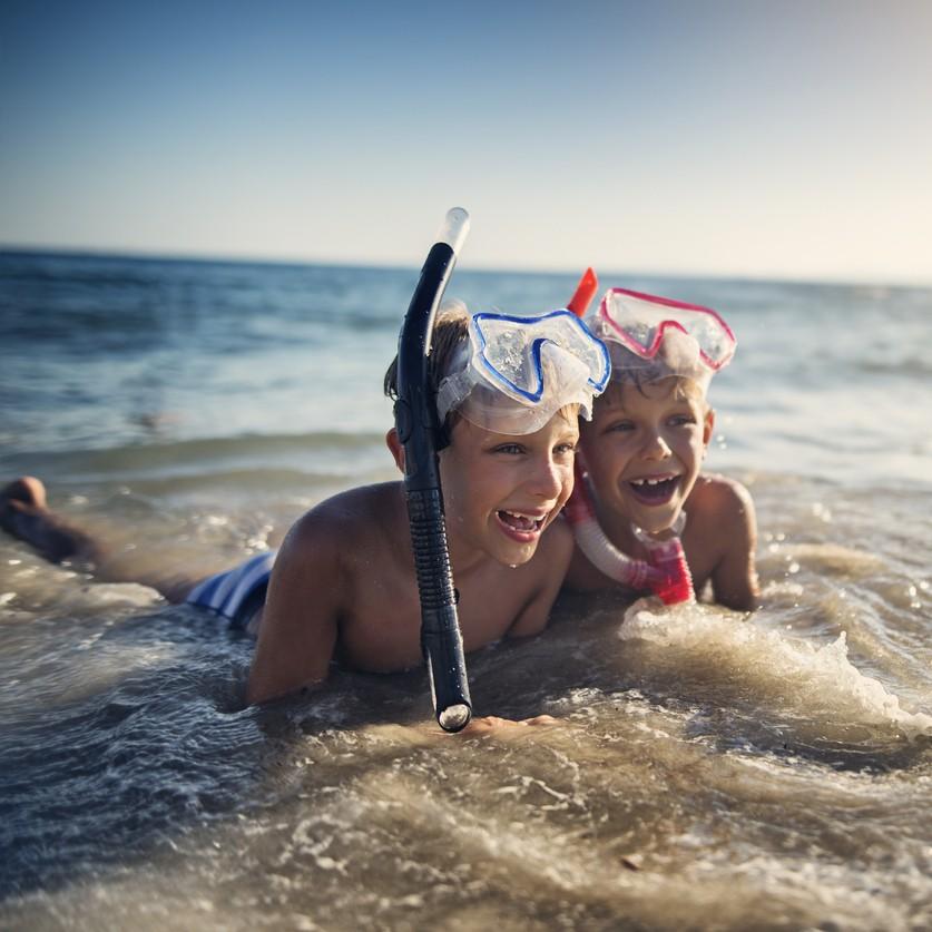Deux enfants équipés de masques et tubas jouant dans l’eau au bord de la mer.